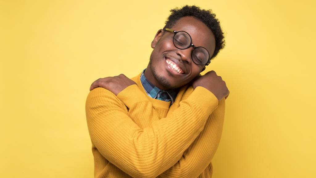 This is an image on a yellow background of a man hugging himself. This is to depict self-regard. 